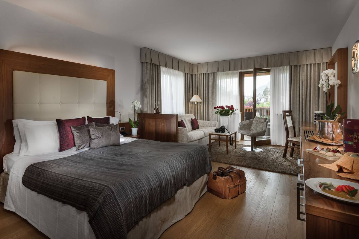 Ruime hotelkamer met groot bed, zithoek met tafel en stoelen, en balkon met uitzicht.