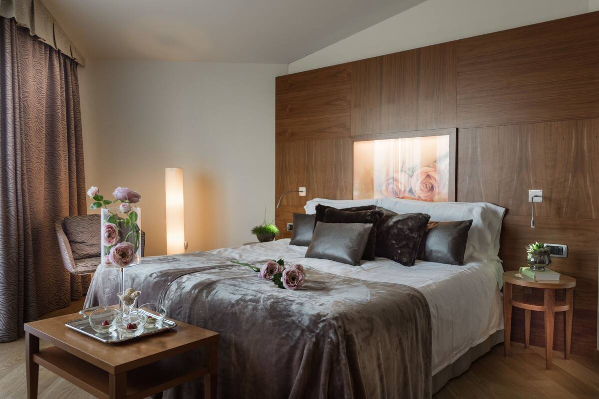 Een stijlvol ingerichte hotelkamer met een groot bed, een houten hoofdeinde, een nachtkastje met een lamp en een klein bijzettafeltje met een plant.