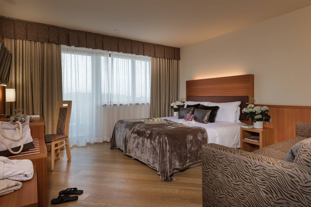Een hotelkamer met een groot bed, een kleinere bank, een bureau met lamp en een stoel.