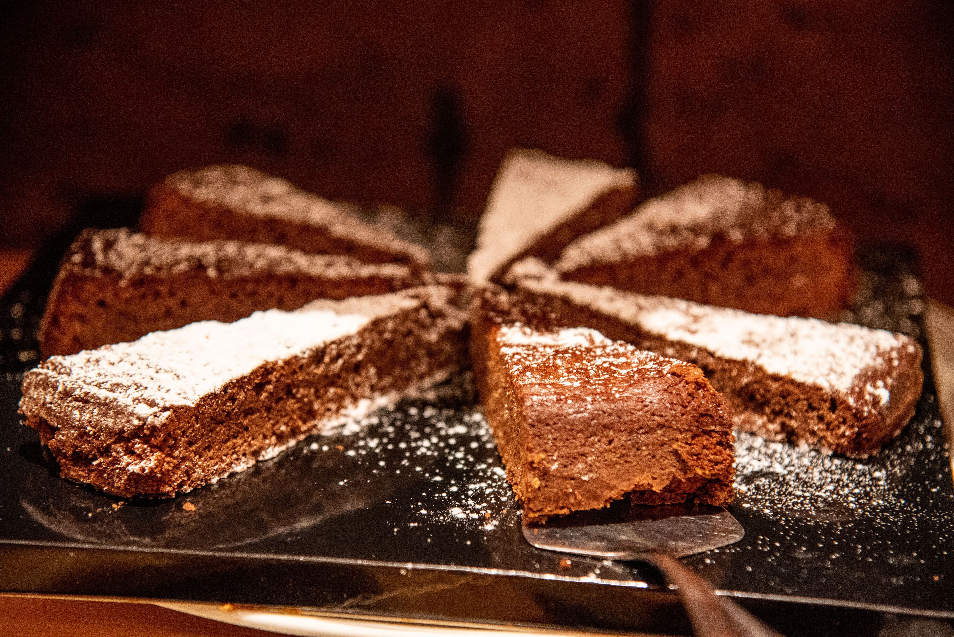 A round cake with a dusting of powdered sugar on top, placed on a black tray.