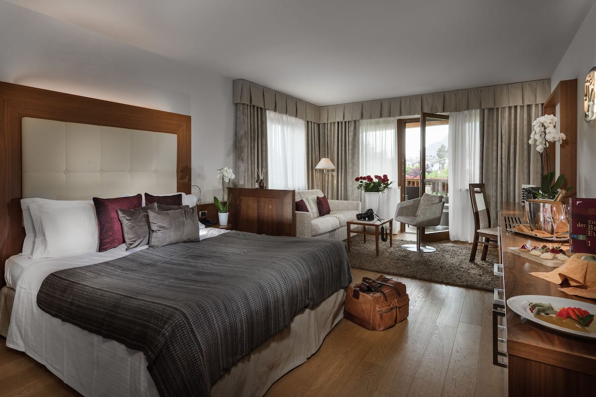 Ruime hotelkamer met een groot bed, een zithoek met een tafel, en een balkon met uitzicht.