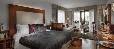 A spacious hotel room with a large bed, a sitting area with a table, and a balcony with a view.