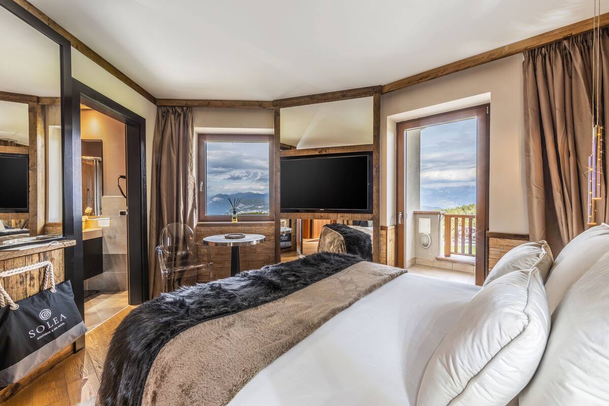 Een hotelkamer met een groot bed, een televisie, een klein tafeltje en een balkon met uitzicht.
