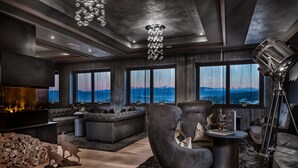 Un salon moderne doté d’une cheminée, de canapés en cuir et d’une grande fenêtre donnant sur les montagnes.