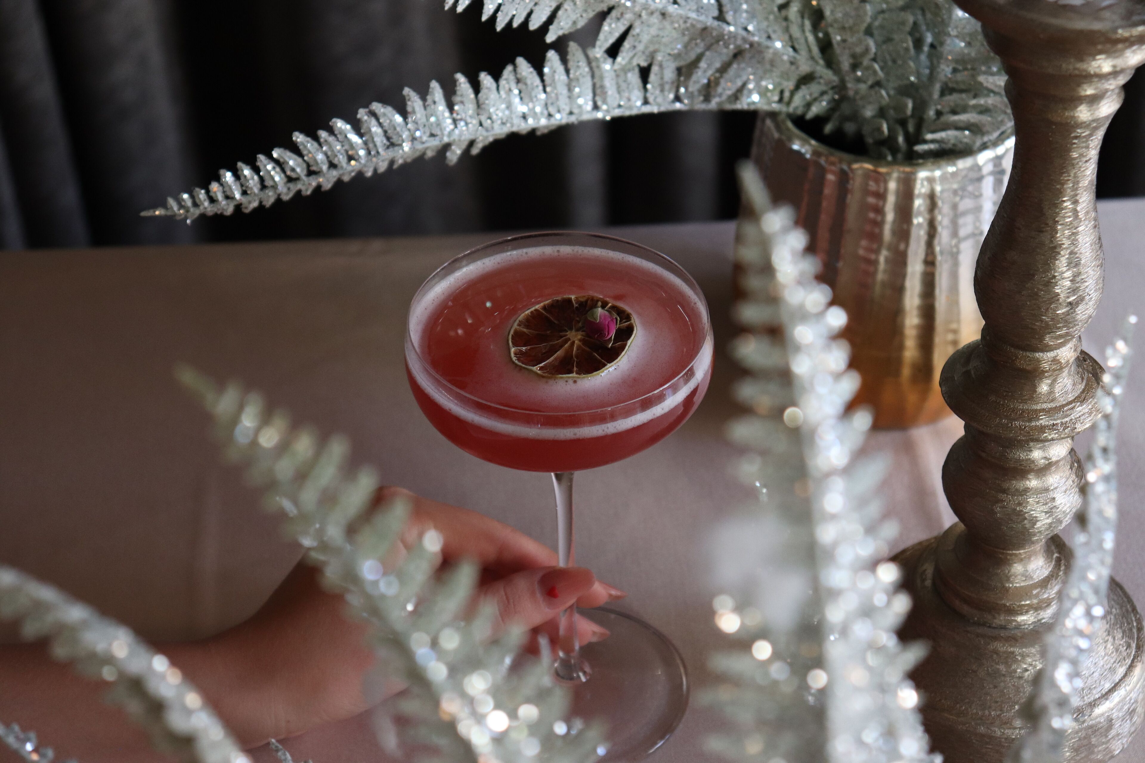 A cocktail glass with a garnish on a table with a decorative plant and a candle.