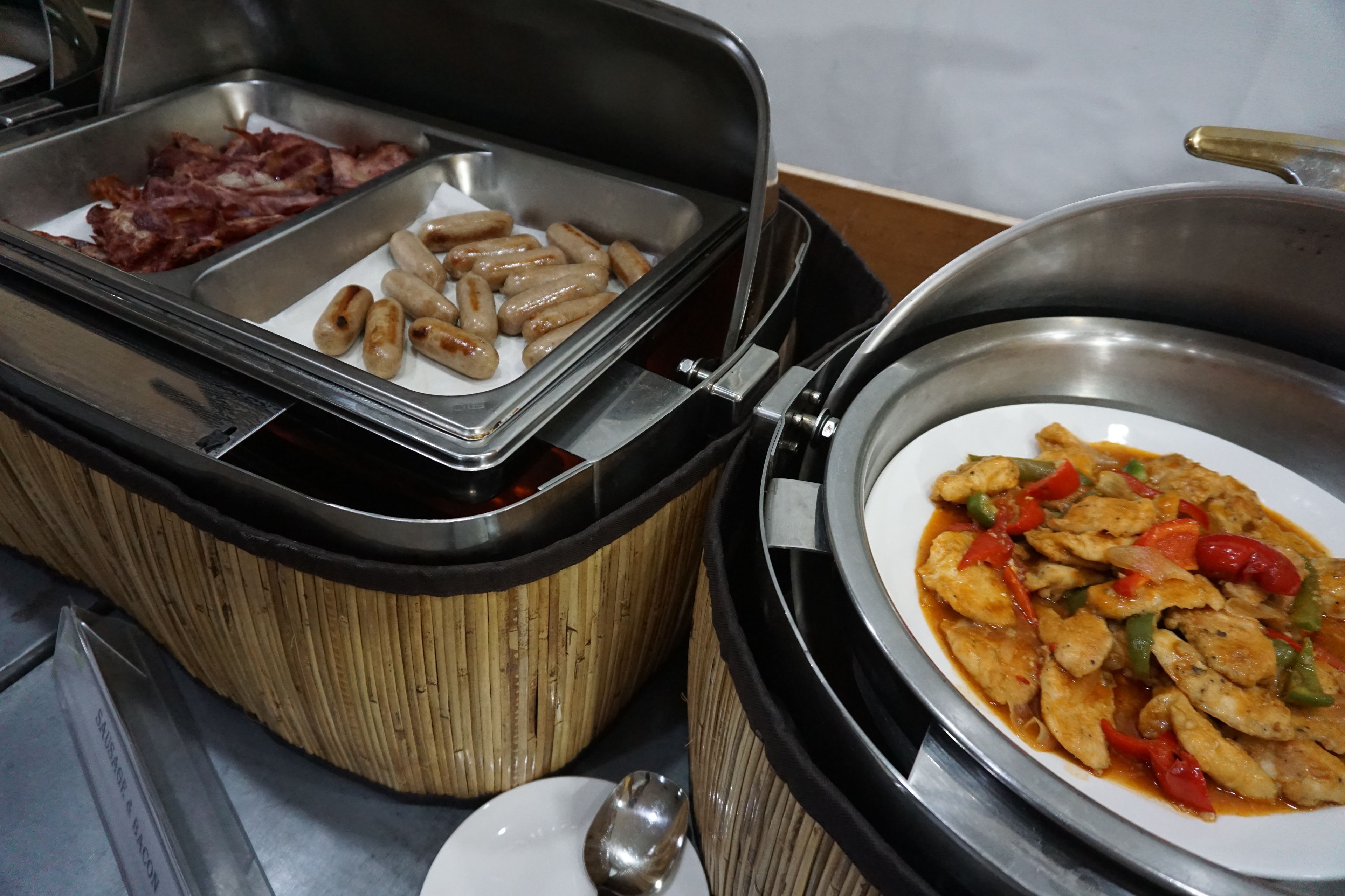 A buffet with various food options including sausages, bacon, and a dish with chicken and vegetables.