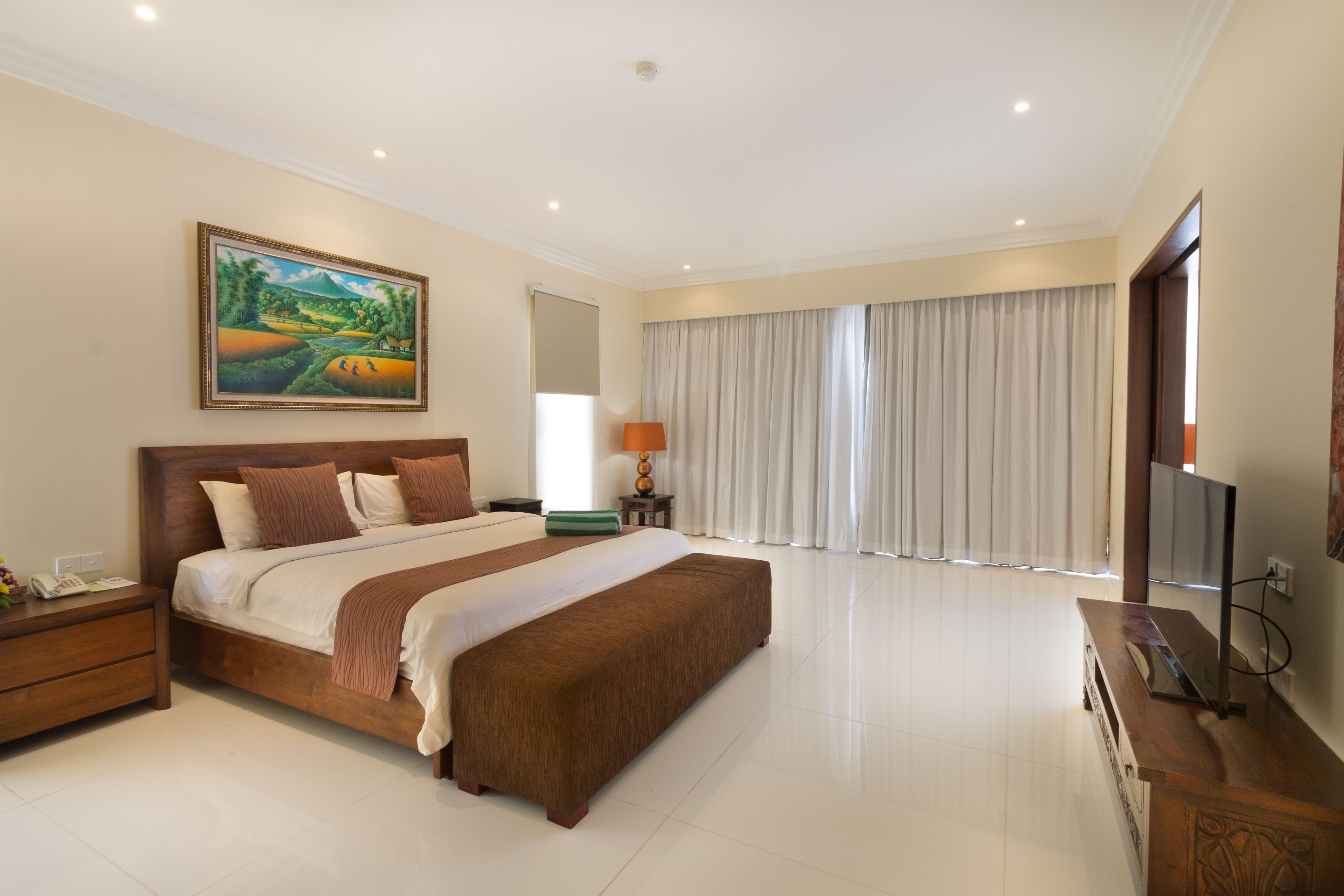 Un dormitorio amplio con una cama grande, un televisor de pantalla plana y un cuadro en la pared.