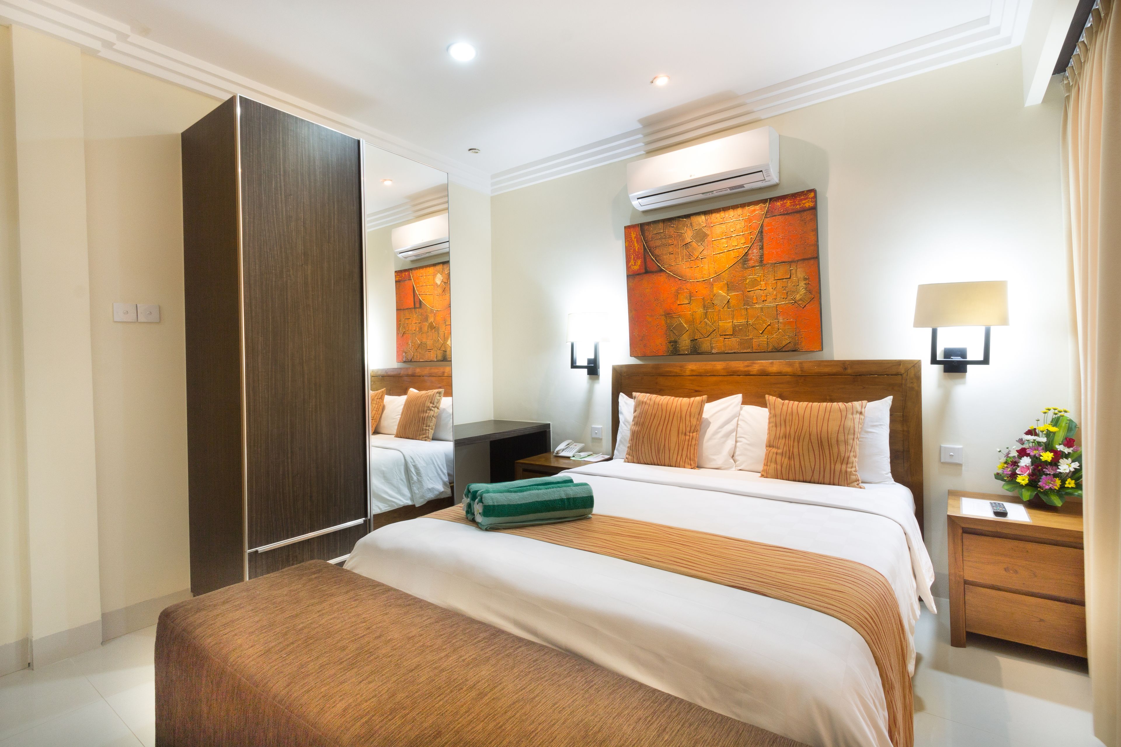 Una habitación de hotel con una cama grande, un armario, una mesita de noche con lámpara y un aire acondicionado instalado en la pared.
