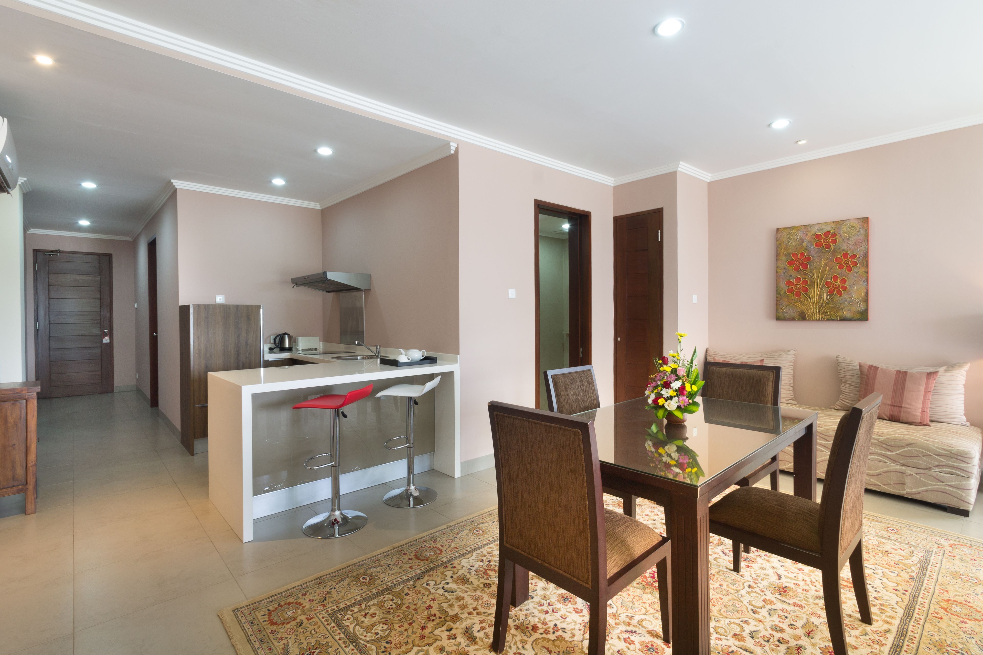 A modern kitchen with a central island, a dining area with a glass table, and a living room with a sofa and a painting.