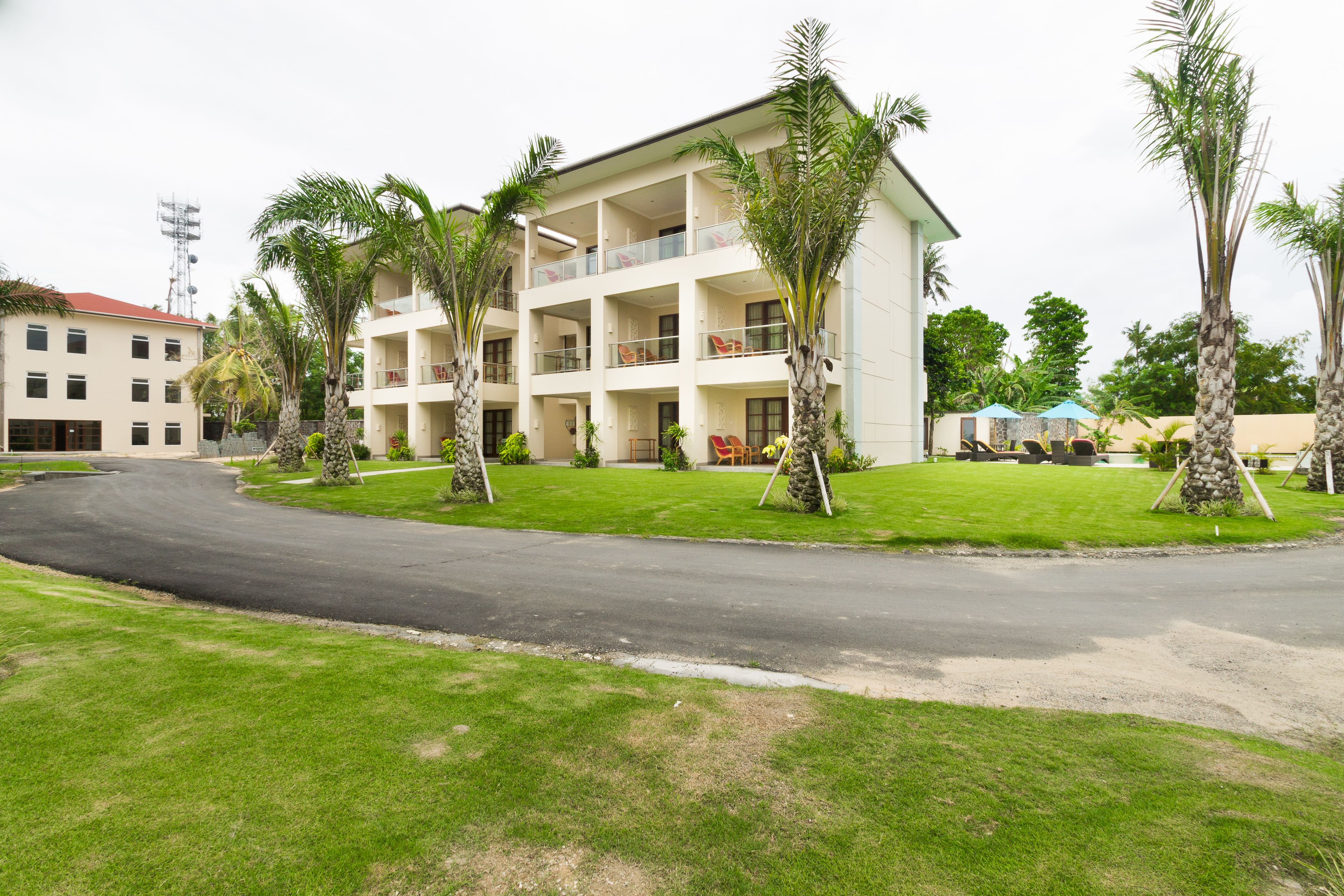 Un hôtel à plusieurs étages doté d’une cour intérieure, entouré de palmiers et accessible par une allée sinueuse.