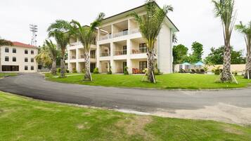 Un hôtel à plusieurs étages doté d’une cour intérieure, entouré de palmiers et accessible par une allée sinueuse.