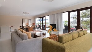 Een ruime woonkamer met een grote bank, een salontafel en een televisie. Er is een balkon met tuinmeubilair en uitzicht op de omgeving.