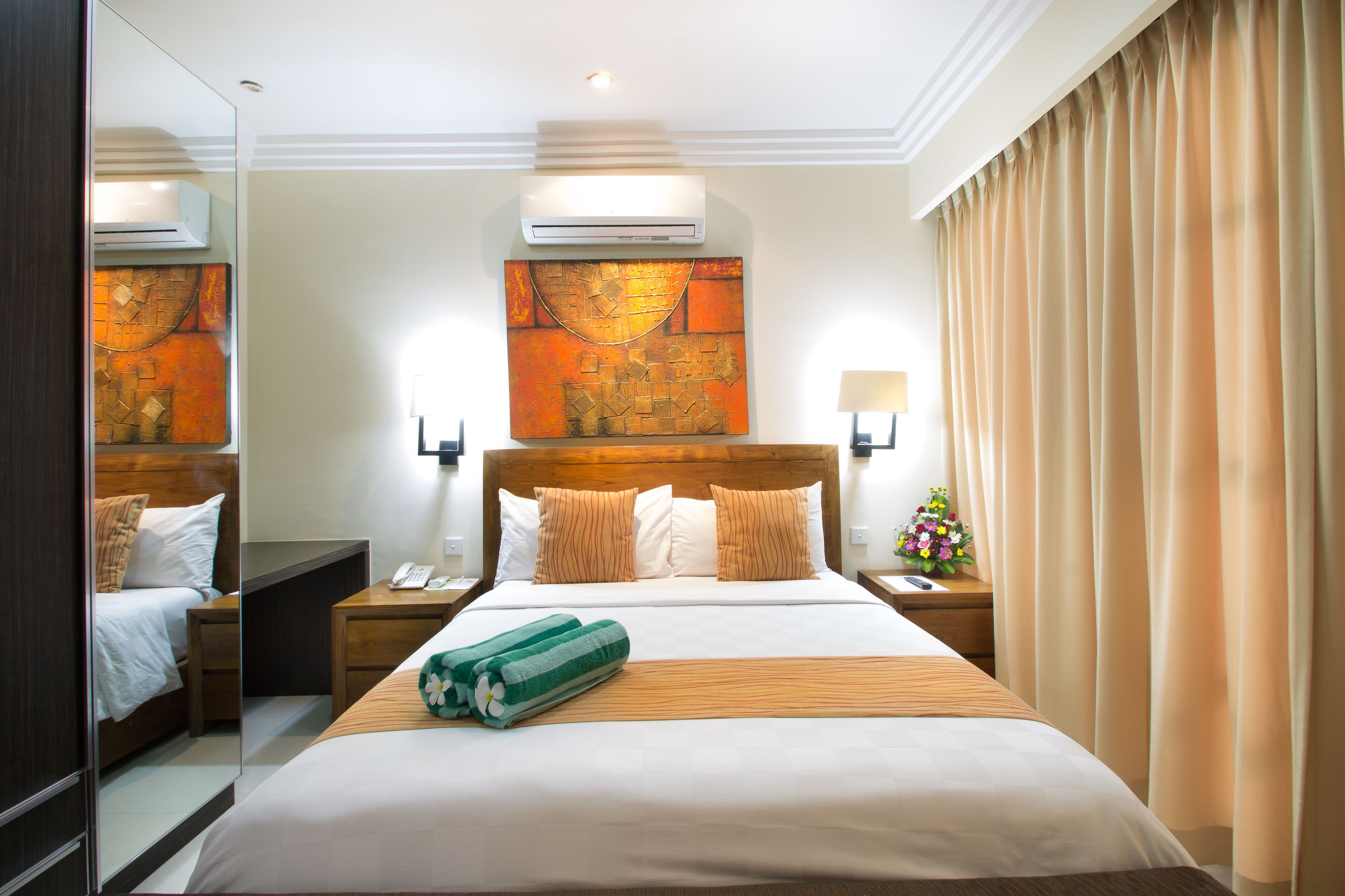 Habitación de hotel con una cama grande, una mesita de noche, un espejo, un equipo de aire acondicionado y una obra de arte colgada en la pared.