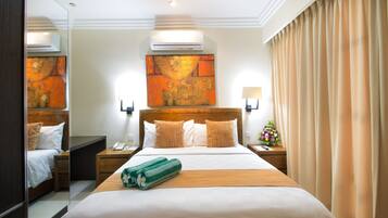 Habitación de hotel con una cama grande, una mesita de noche, un espejo, un equipo de aire acondicionado y una obra de arte colgada en la pared.
