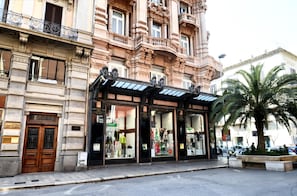 Um edifício histórico com arquitetura elaborada, entrada coberta e uma palmeira ao primeiro plano.
