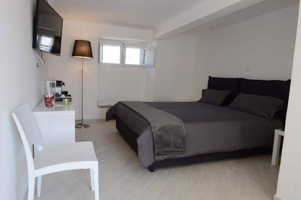 Un dormitorio con una cama, un televisor en la pared, un escritorio con silla y una lámpara de pie.