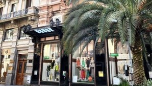 Un bâtiment historique à l’architecture riche et ornée, un palmier au premier plan et une vitrine avec des mannequins.