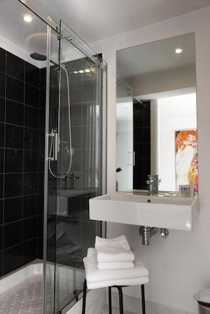 Uma casa de banho moderna com chuveiro envolto em vidro, uma pia branca e um espelho grande.