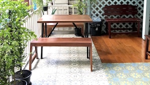 Un patio cubierto con mesa y banco de madera, plantas en macetas y piso con diseño.