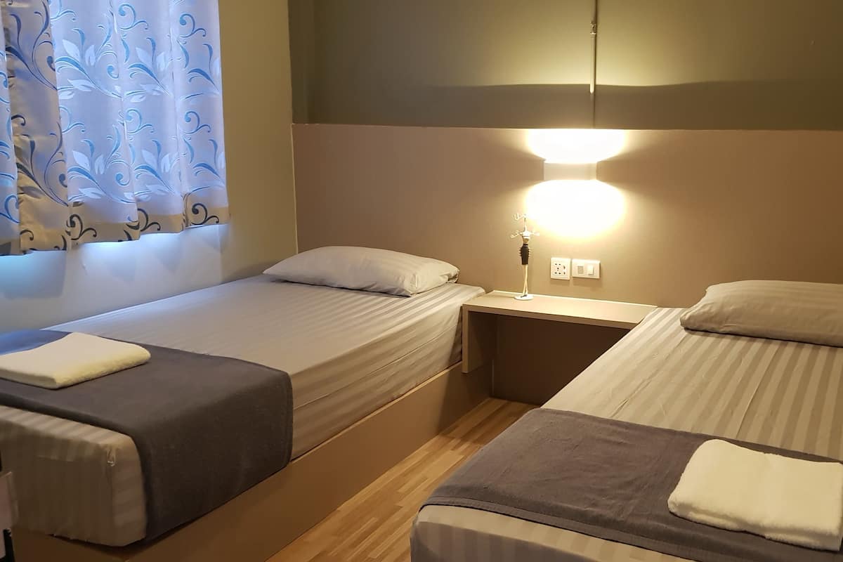 Une chambre avec deux lits simples, chacun étant équipé d’un oreiller et d’une couverture. Une table de chevet avec une lampe se trouve entre les deux lits.