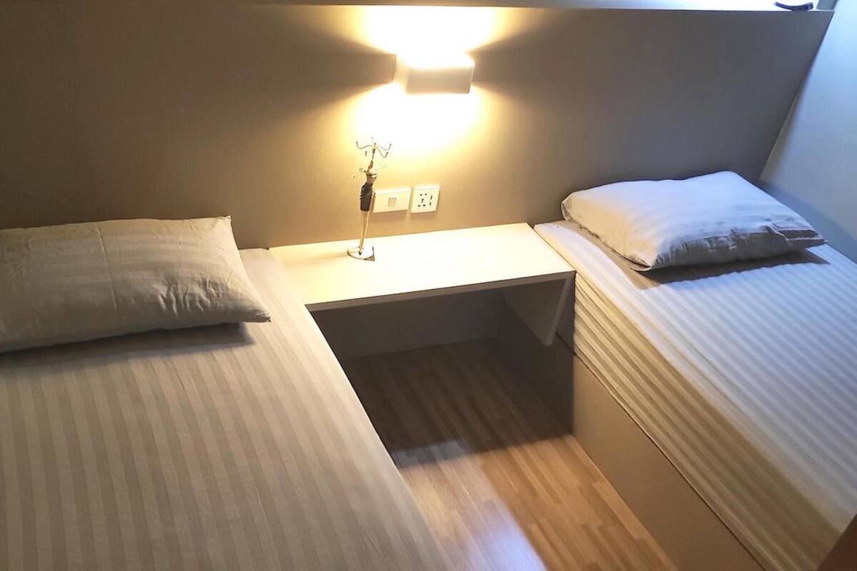 Une petite pièce, de taille modeste, comprenant deux lits, une table de chevet et une lampe fixée au mur.