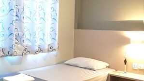 Habitación de hotel con dos camas, una ventana con cortinas estampadas, una mesita de noche con lámpara y un aire acondicionado instalado en la pared.