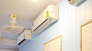 Un pasillo con paredes azules, piso de madera y puertas blancas. Hay dos ventiladores de techo y dos aires acondicionados instalados en la pared.