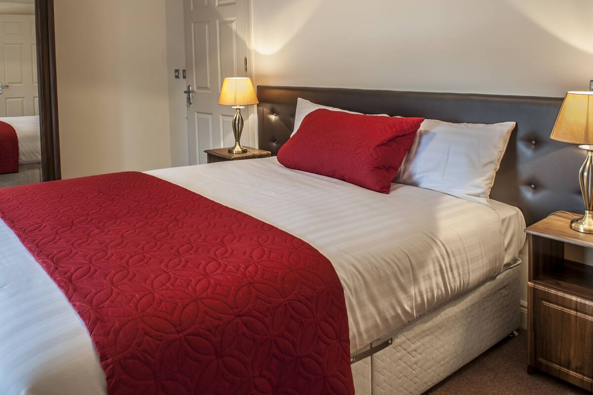 Un lit bien fait, recouvert d’une couvre-lit rouge et blanche, avec deux lampes de chevet et une table de chevet en bois.