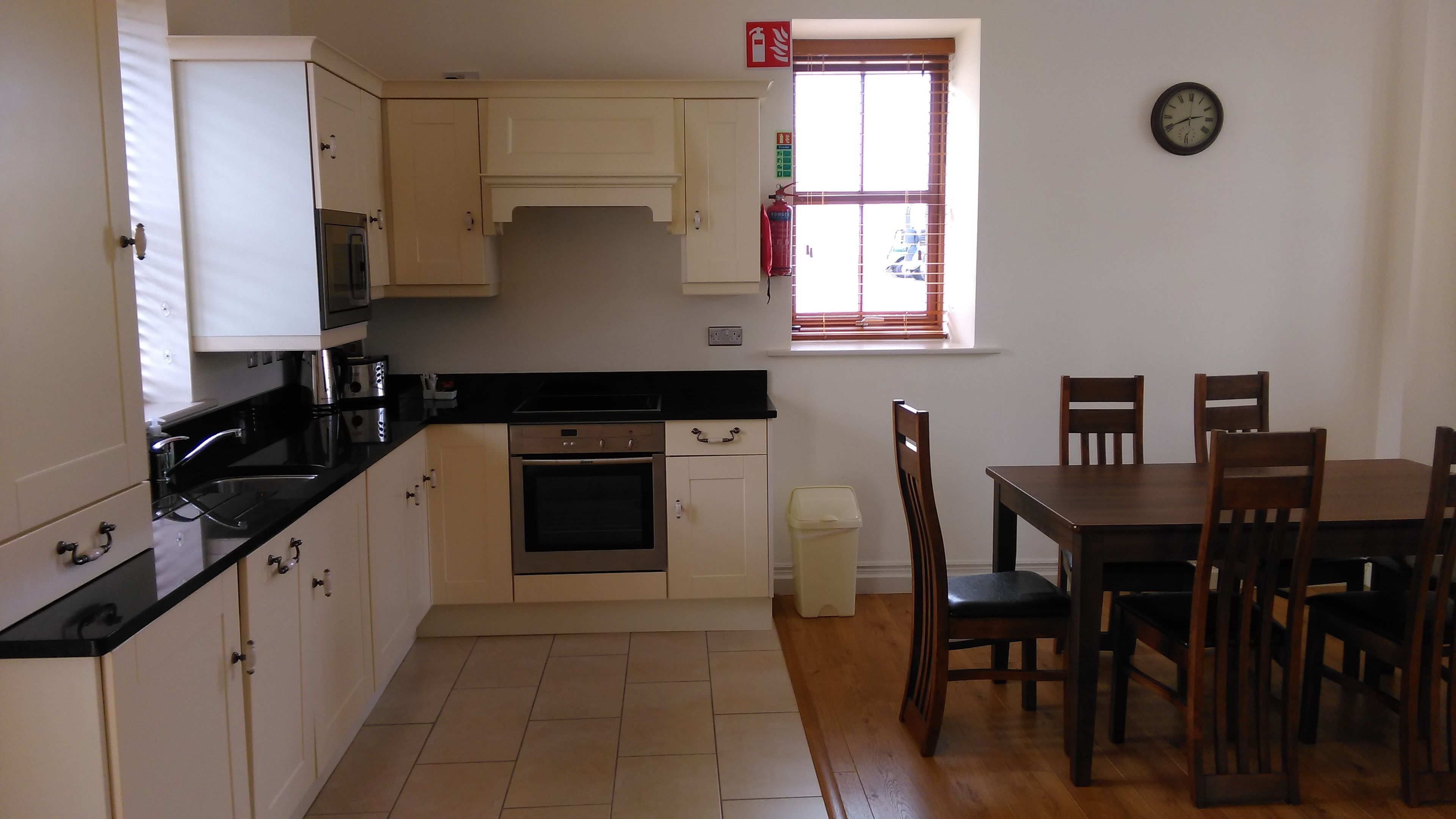 A kitchen with white cabinets, a black countertop, an oven, a trash bin, and a dining table with chairs.