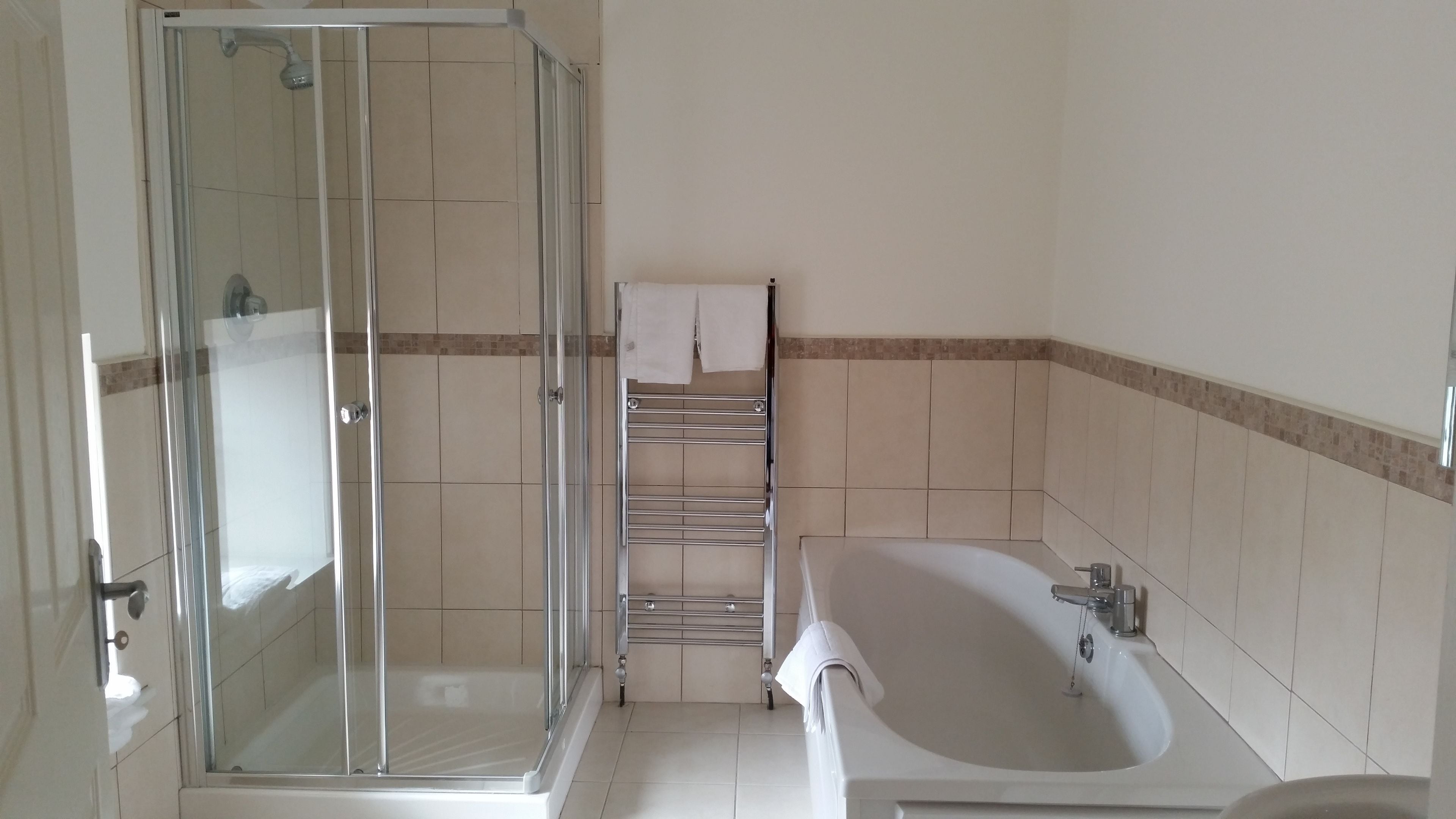 A bathroom with a glass-enclosed shower, a white bathtub, and a towel rack.