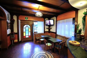 L’intérieur d’un restaurant avec des murs en bois, une porte en vitrail, un téléviseur et un espace repas comprenant des chaises et des tables.