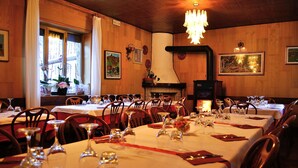 A restaurant with multiple tables set for dining, a fireplace, and wooden walls. - Albergo Ristorante Morandi (Valbondione)