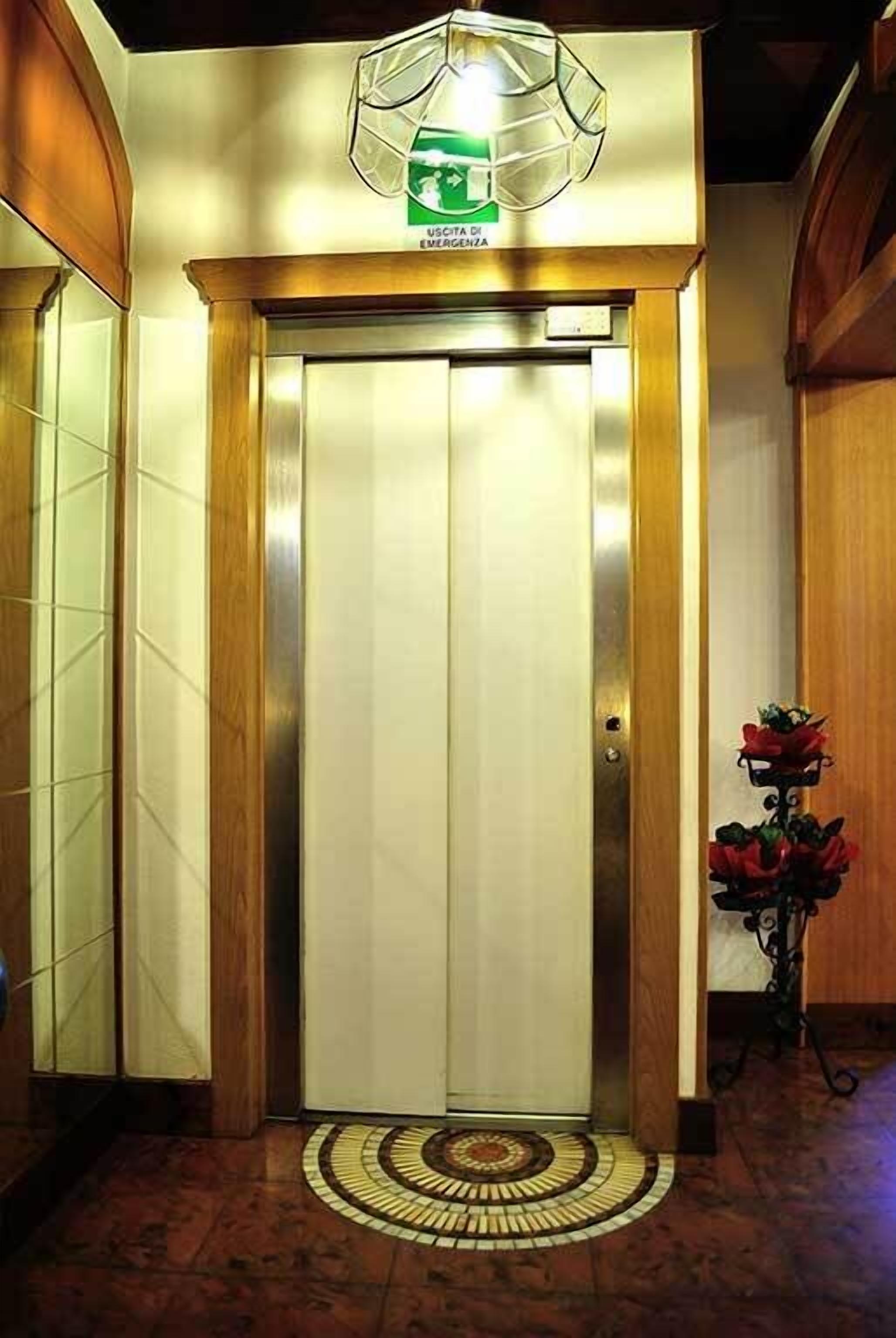 An elevator with a green emergency exit sign, a wooden frame, and a red flower arrangement on the floor.