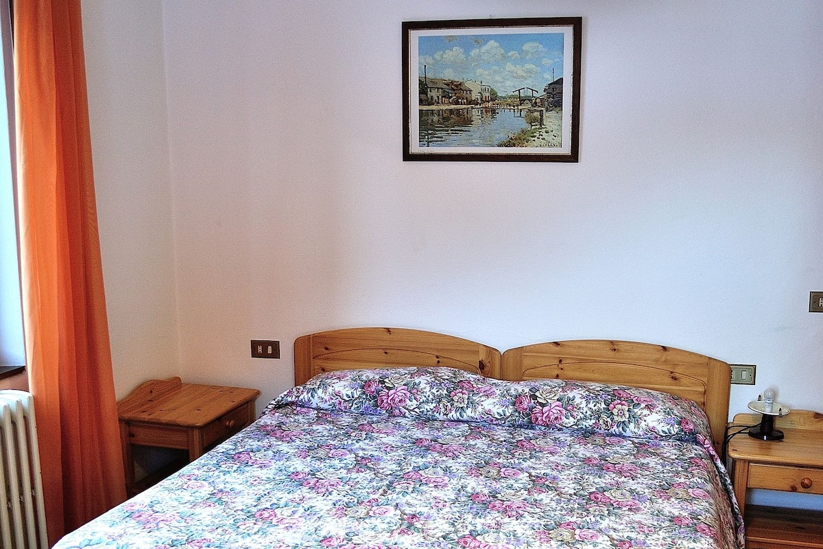A bedroom with a wooden bed, a nightstand, a bedside table, a hanging lamp, and a framed picture on the wall.