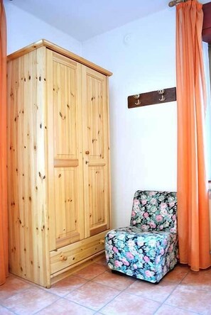 A room with a wooden wardrobe, a floral chair, and orange curtains. - Albergo Ristorante Morandi (Valbondione)