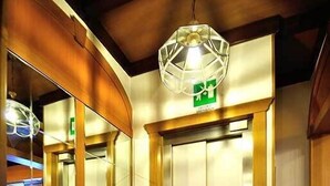 An elevator with a green emergency exit sign, a decorative mirror, and a patterned floor mat. - Albergo Ristorante Morandi (Valbondione)