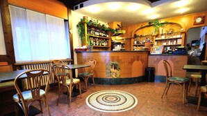 A restaurant interior with wooden furniture, a tiled floor, and a bar area with shelves of bottles and a clock on the wall. - Albergo Ristorante Morandi (Valbondione)