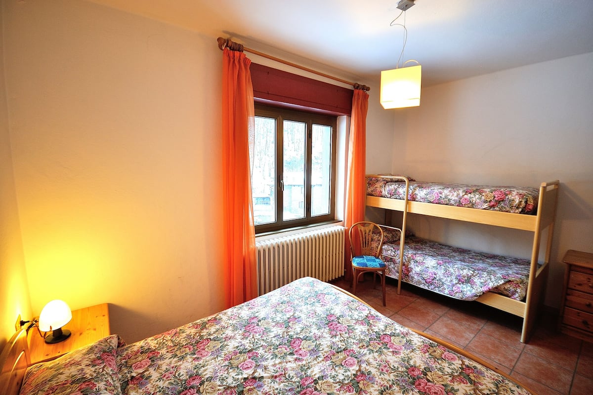 A room with a bed, a chair, a window with curtains, a radiator, and a bunk bed.