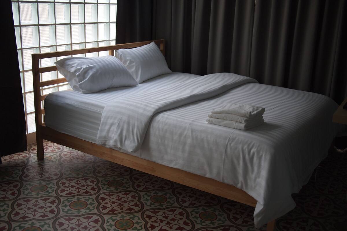 Una cama bien hecha con sábanas blancas y almohadas, un cabecero de madera y un suelo estampado.