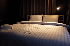 A neatly made bed with striped bedding and pillows, a folded towel on the side, and a window with curtains. - C40Winks Hostel (Bangkok)