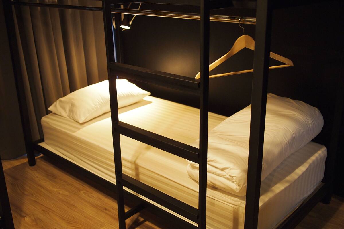 Una cama litera con estructura de madera, ropa de cama blanca y una percha colgante.