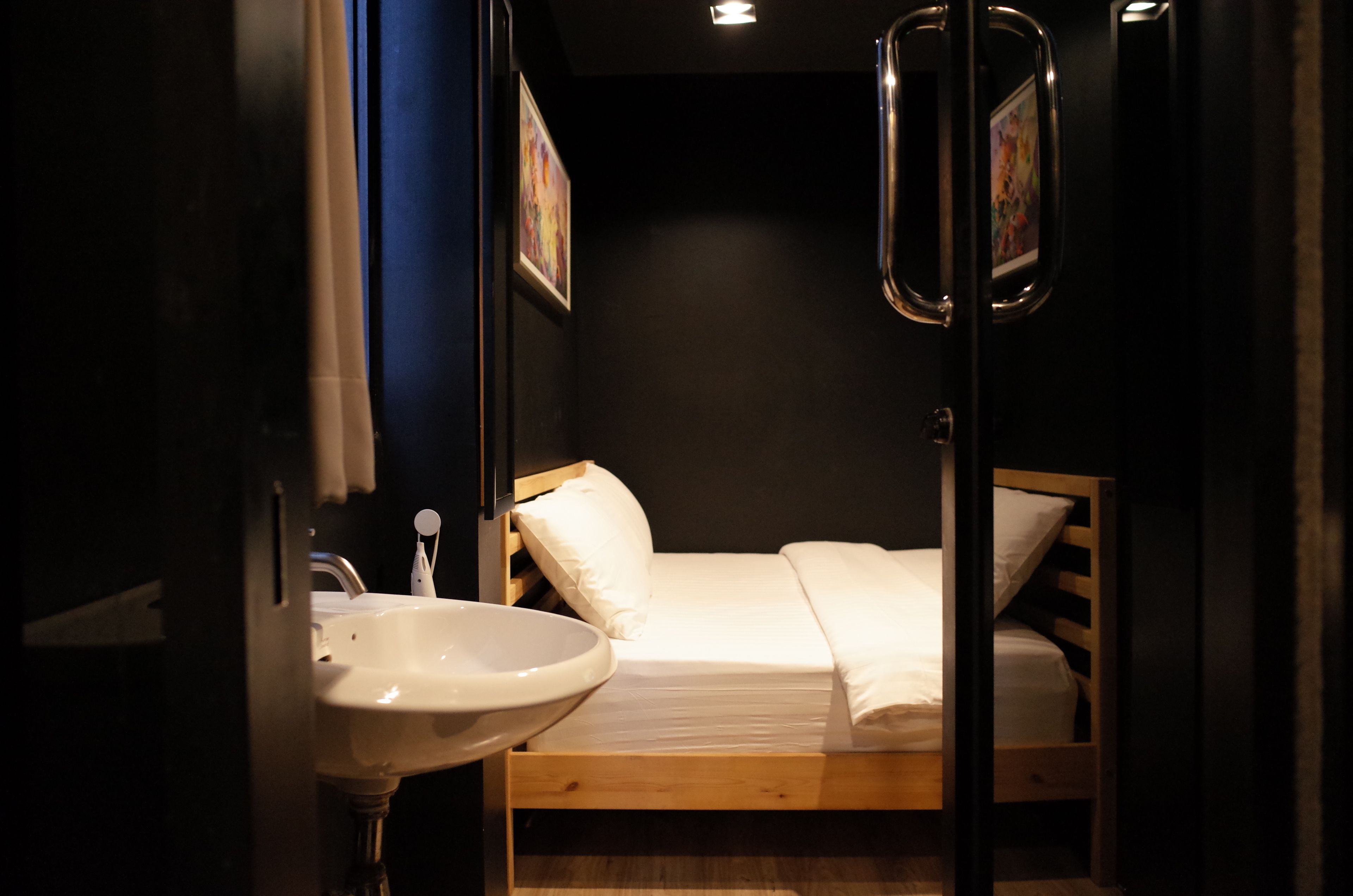 A small, dimly lit room with a wooden bed, a white sink, and a mirror.