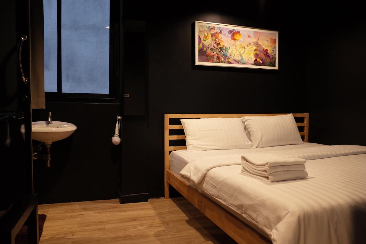 Un dormitorio con cama de madera, ropa de cama blanca, una mesita de noche, un lavamanos blanco y una ventana con vistas.