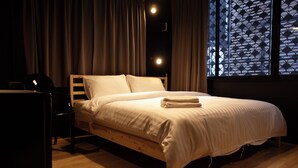 Una cama bien hecha con ropa de cama blanca en una habitación con suelo de madera y una ventana con diseño geométrico.