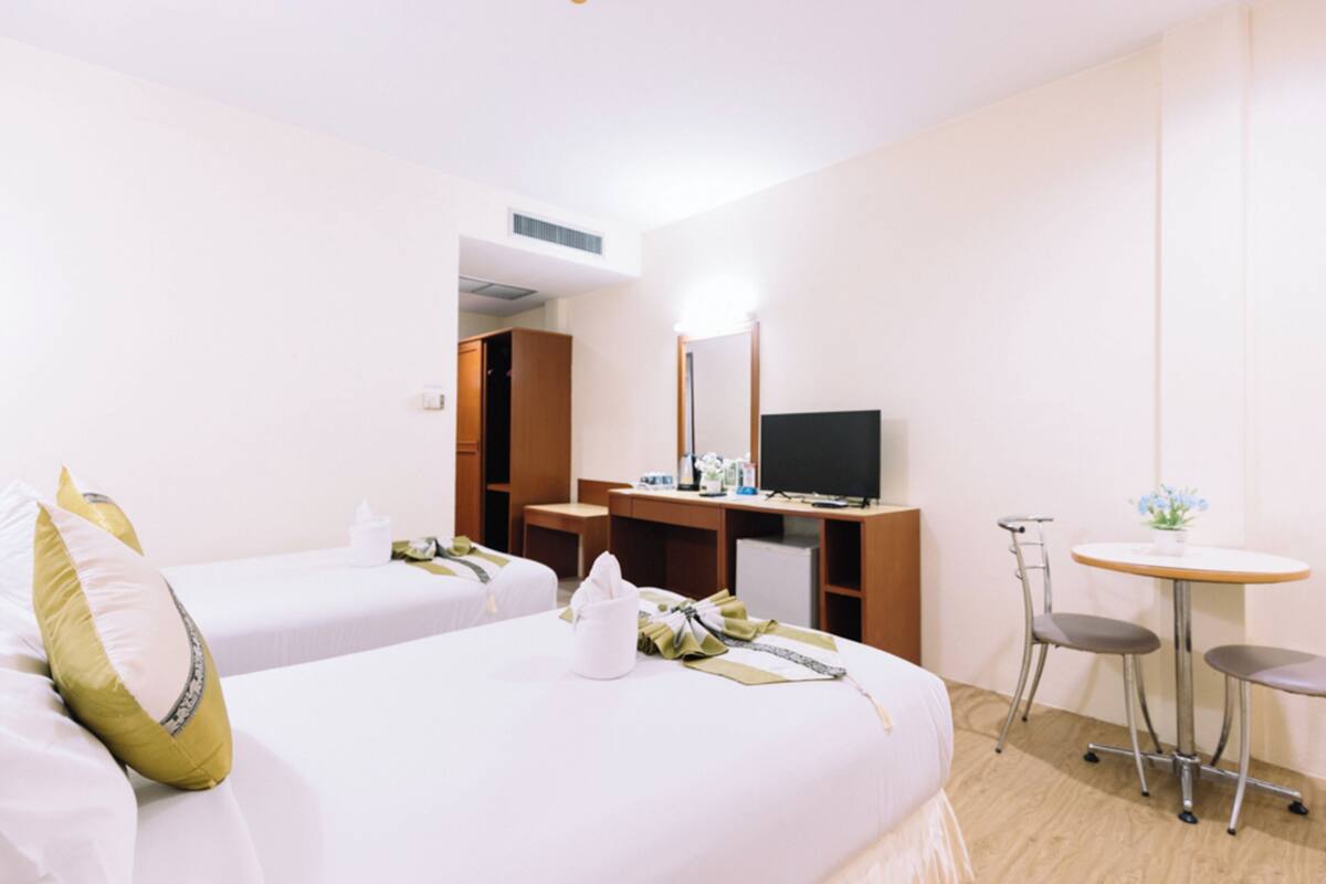 A hotel room with two beds, a desk with a computer, a TV, and a small table with a chair.