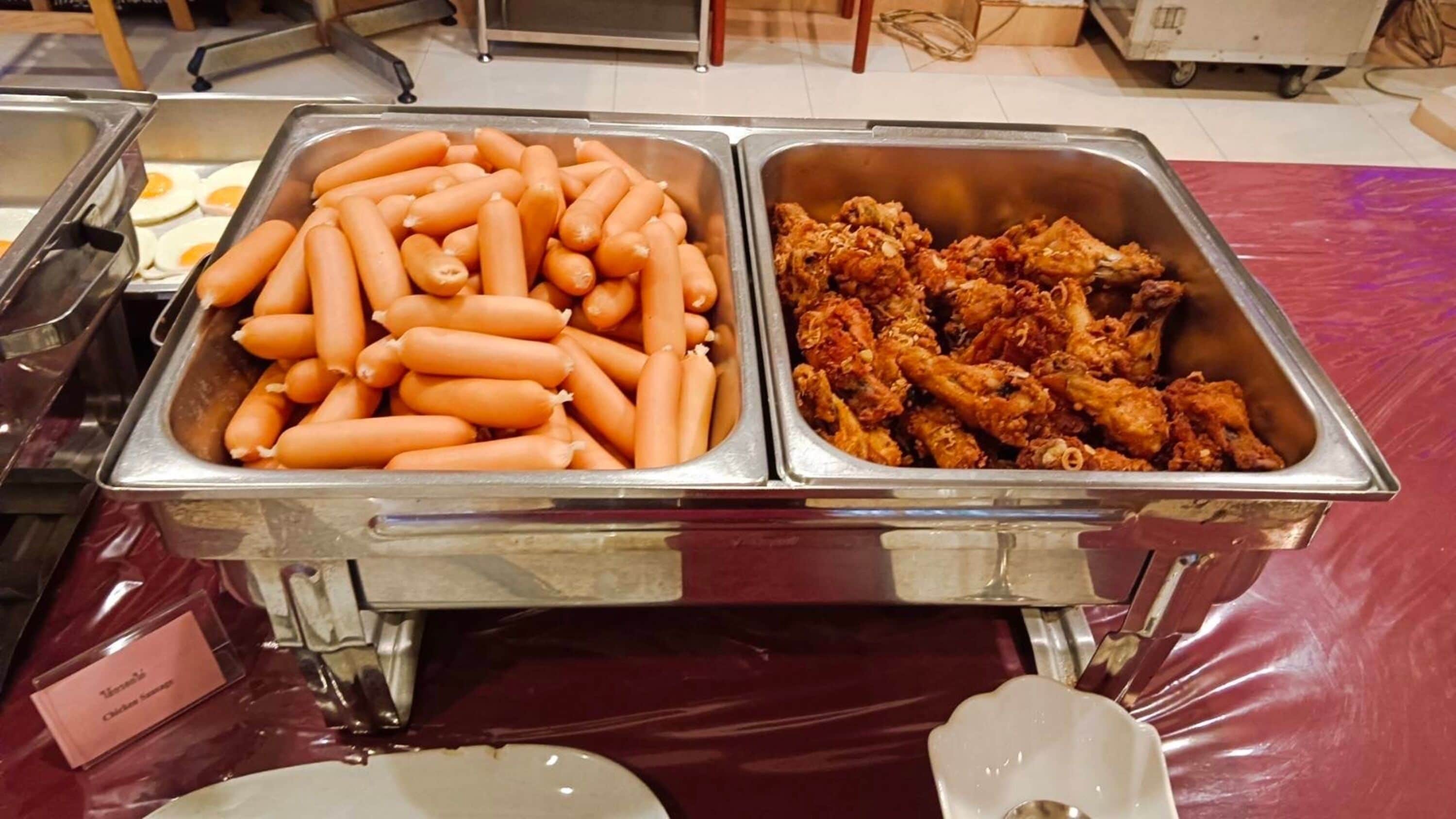 A buffet table with two metal trays, one containing sliced boiled eggs and the other with fried chicken wings.