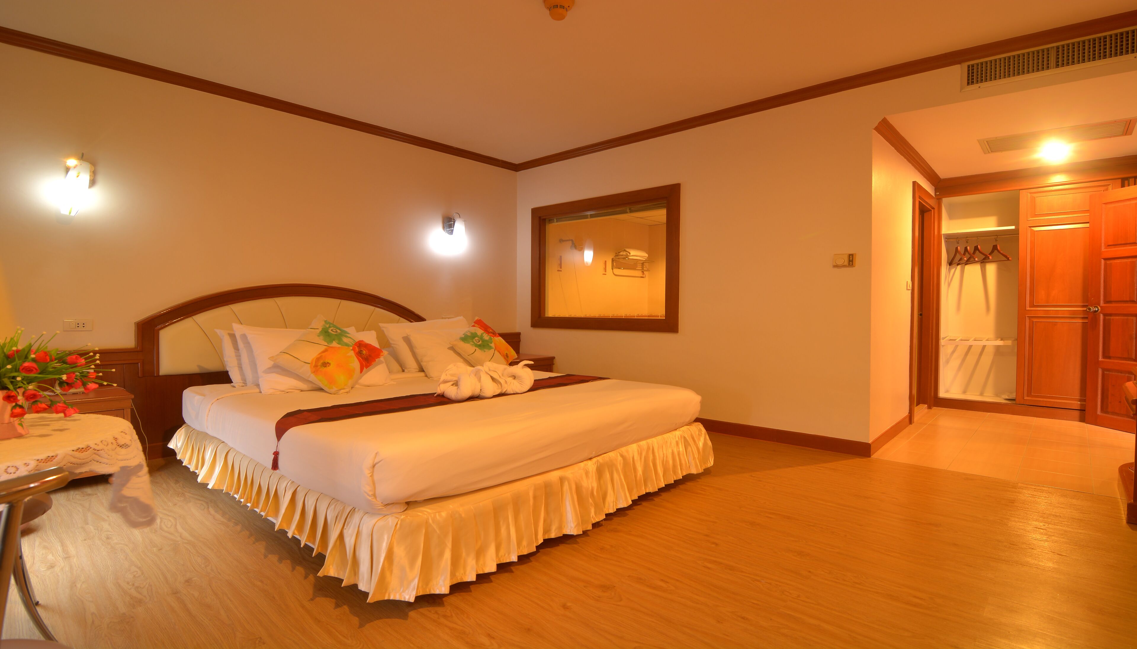 Una habitación de hotel con una cama grande, una mesita de noche con un florero, un espejo y un armario de madera.