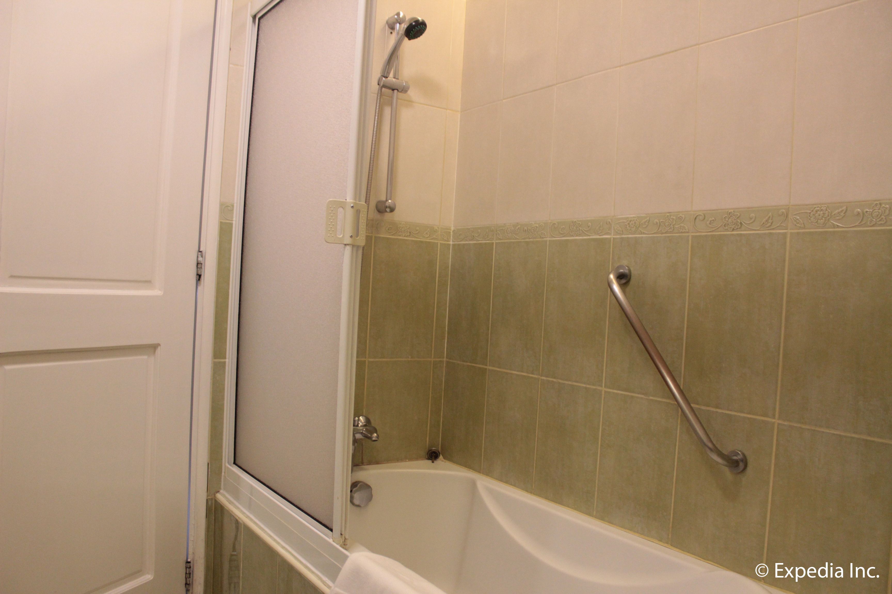 A bathroom with a bathtub, a shower, and a handrail.