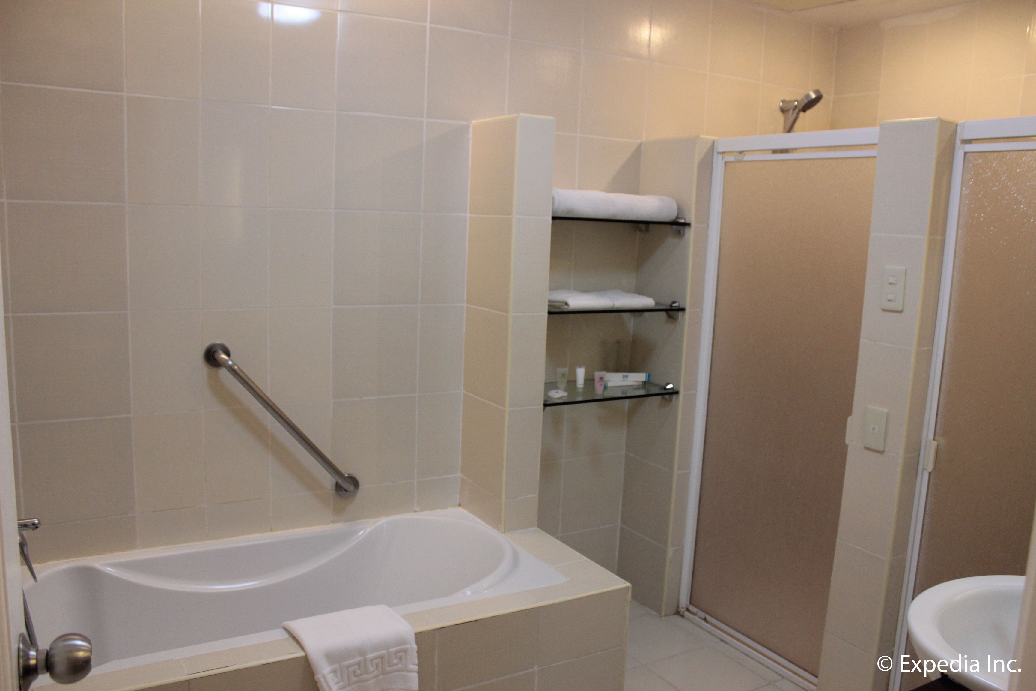 A bathroom with a bathtub, a shower, and a toilet. There is a glass shelf with toiletries.