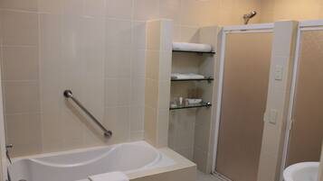 A bathroom with a bathtub, a shower, and a toilet. There is a glass shelf with toiletries.